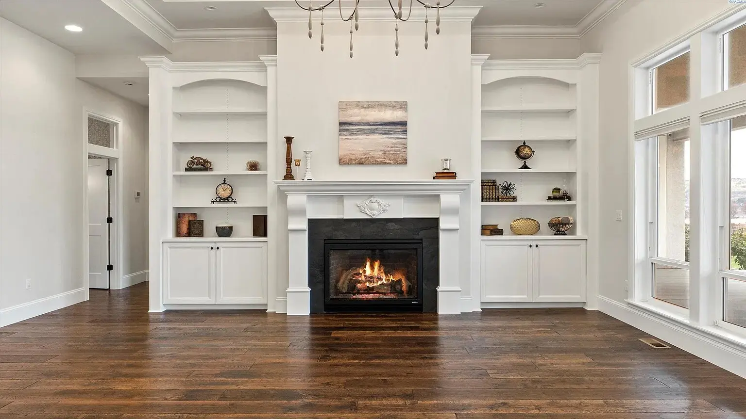 Living room with a lit fireplace, white built-in shelves, and hardwood floors.