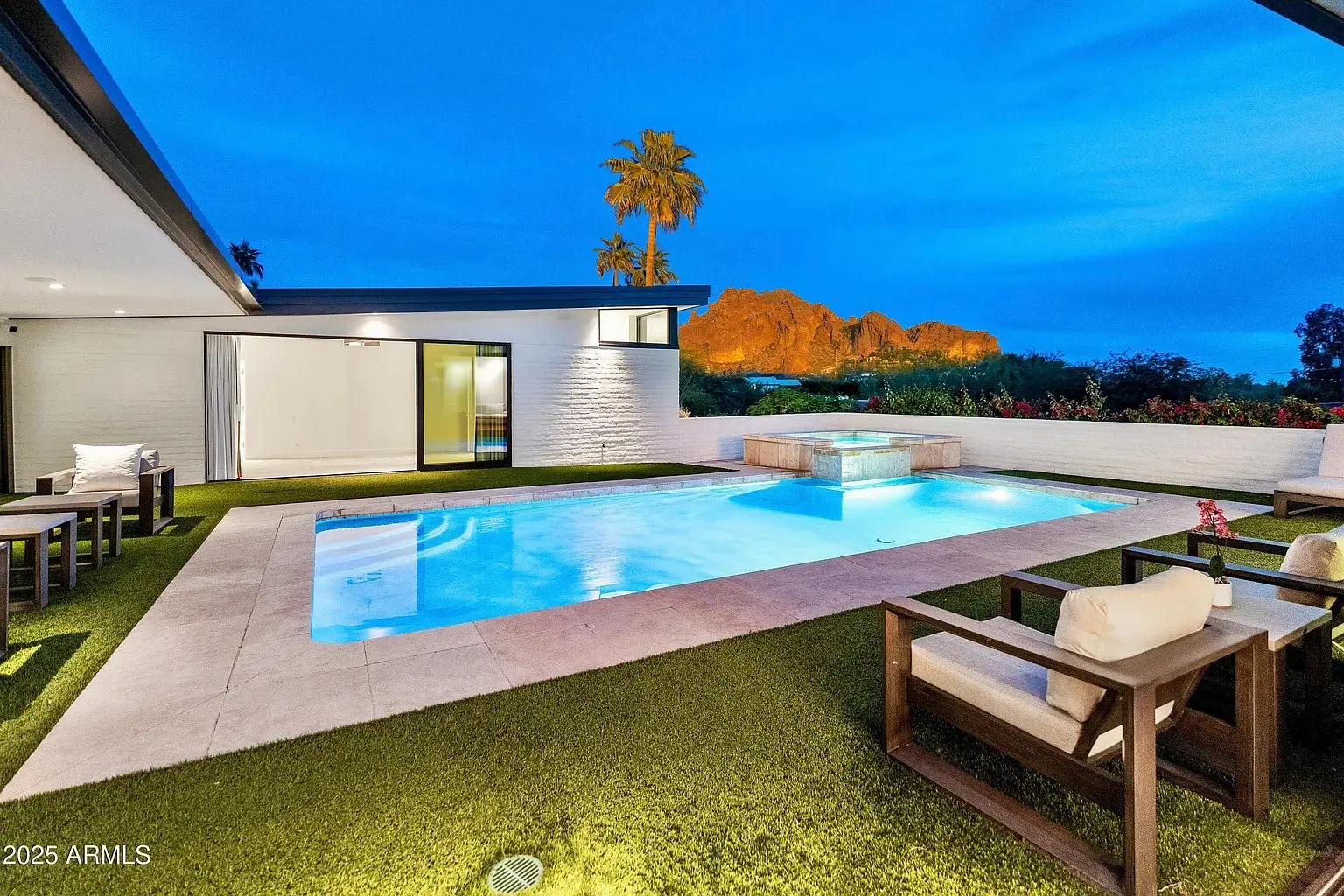 Modern backyard with a pool, patio furniture, and a view of mountains at sunset.