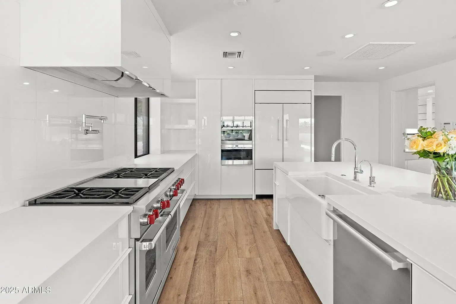 Modern kitchen with white cabinets, stainless steel appliances, wooden floor, and a vase of yellow roses.
