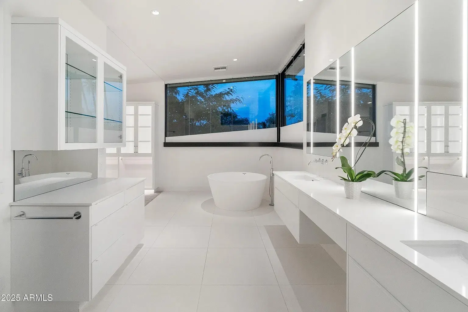 Modern white bathroom with large bathtub, double sinks, and large windows.