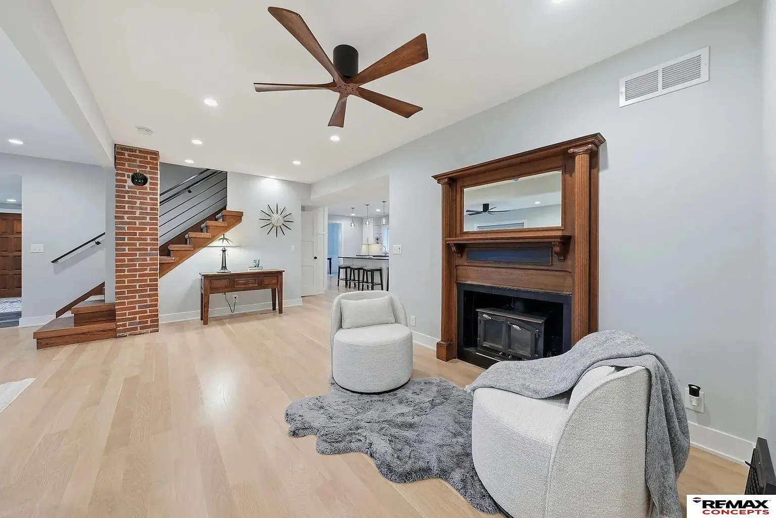 Modern living room with two chairs, fireplace, ceiling fan, and open staircase.