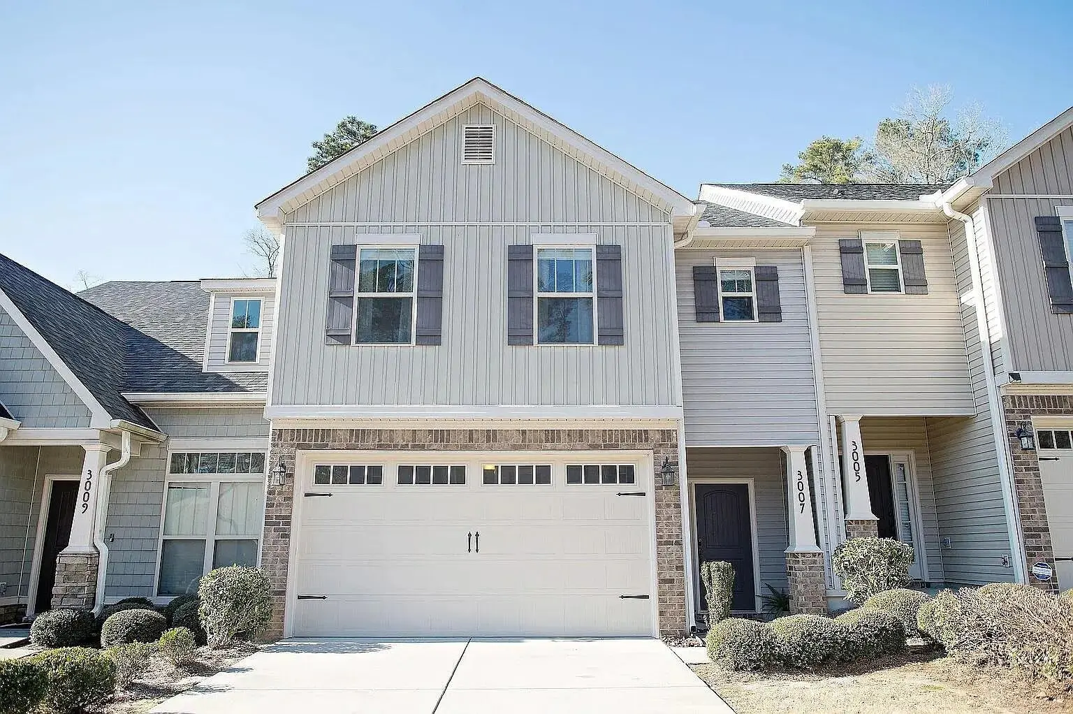 Two-story townhouse with a double garage, light siding, and small shrubs in front.