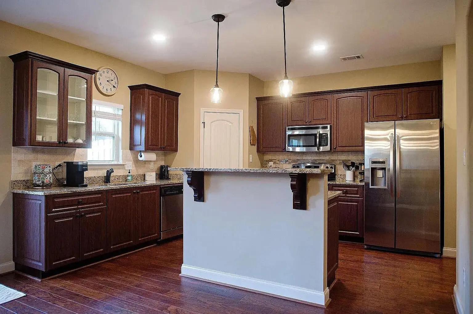 Modern kitchen with dark wood cabinets, stainless steel appliances, and pendant lighting over a central island.