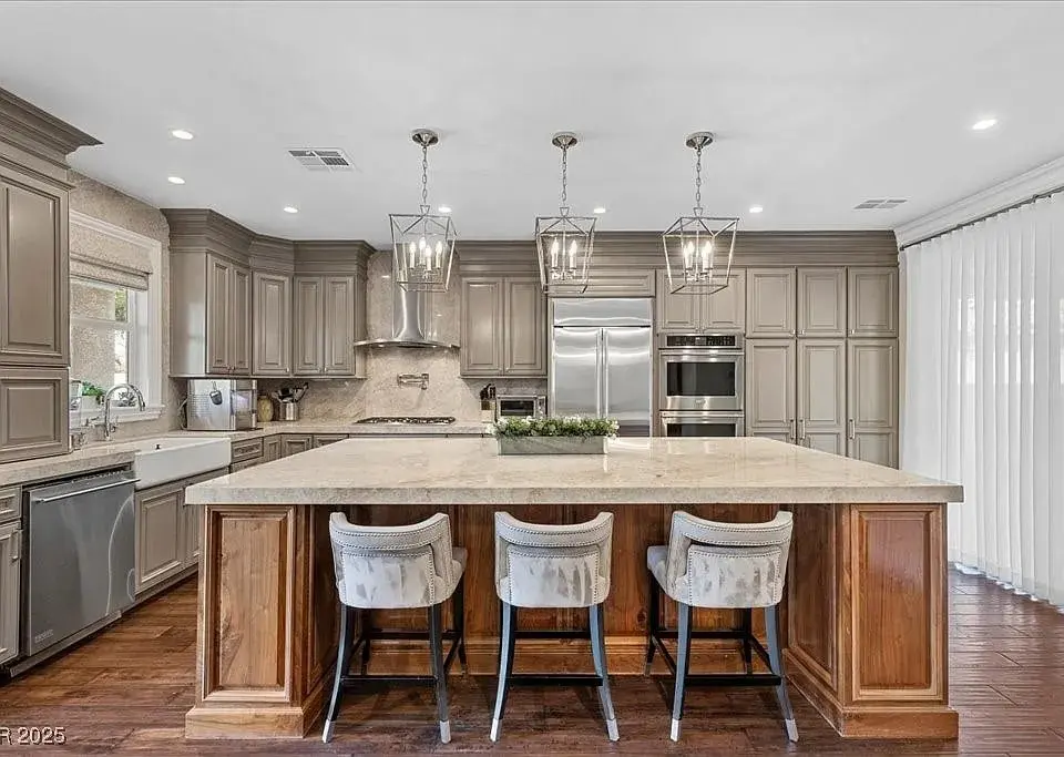 Spacious modern kitchen with large island, barstools, stainless steel appliances, and pendant lighting.