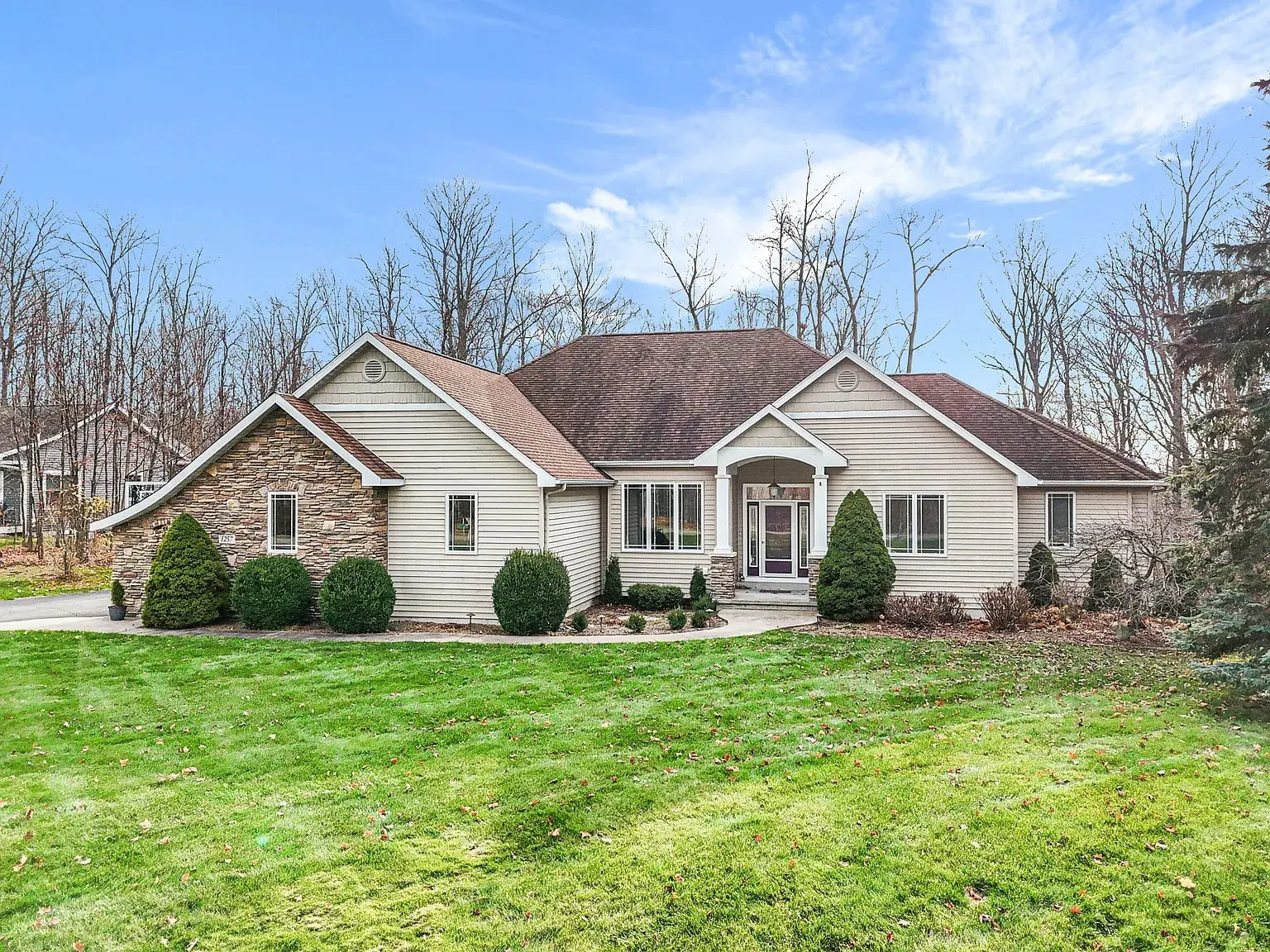Single-story house with stone and siding exterior, surrounded by grass and bare trees.