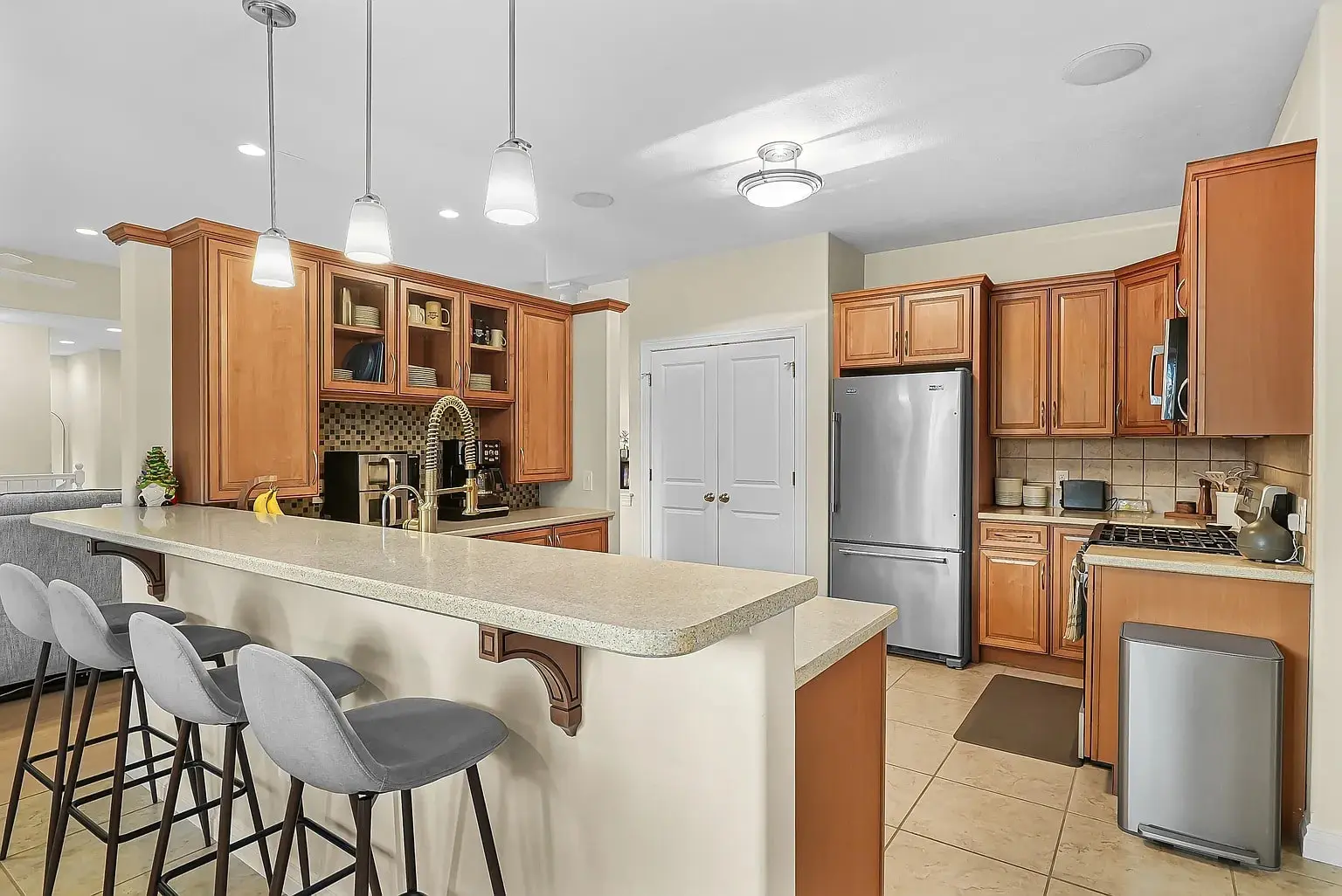Modern kitchen with wooden cabinets, stainless steel appliances, and a breakfast bar with four gray stools.