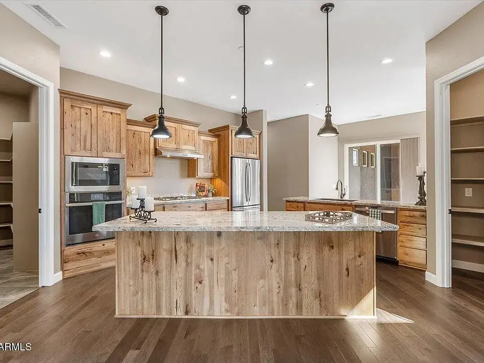 Modern kitchen with wooden cabinets, large island, stainless steel appliances, and pendant lighting.