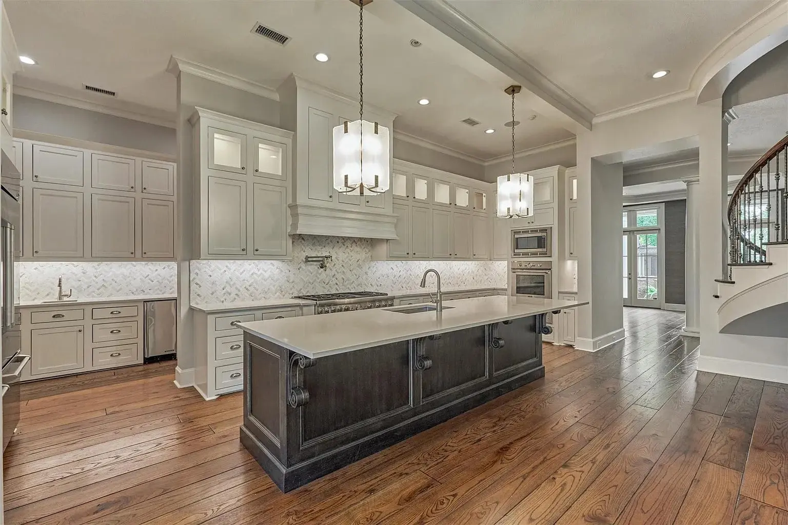 Spacious modern kitchen with large island, pendant lights, white cabinets, and hardwood floors.