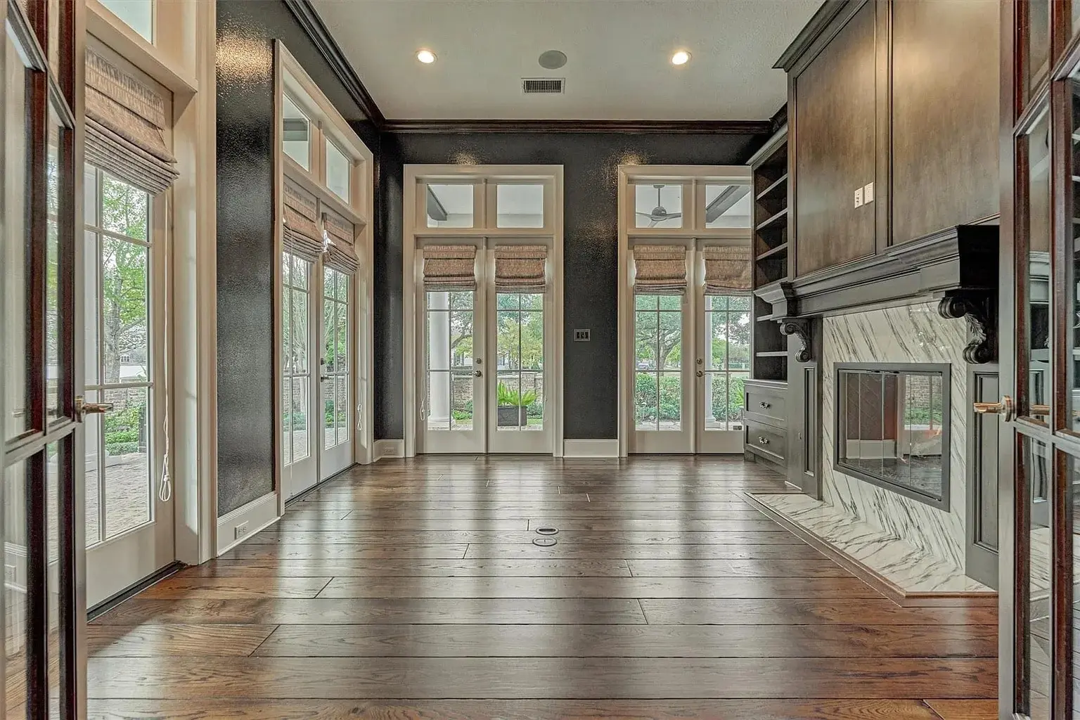 Spacious room with dark wood floors, large windows, and a marble fireplace.