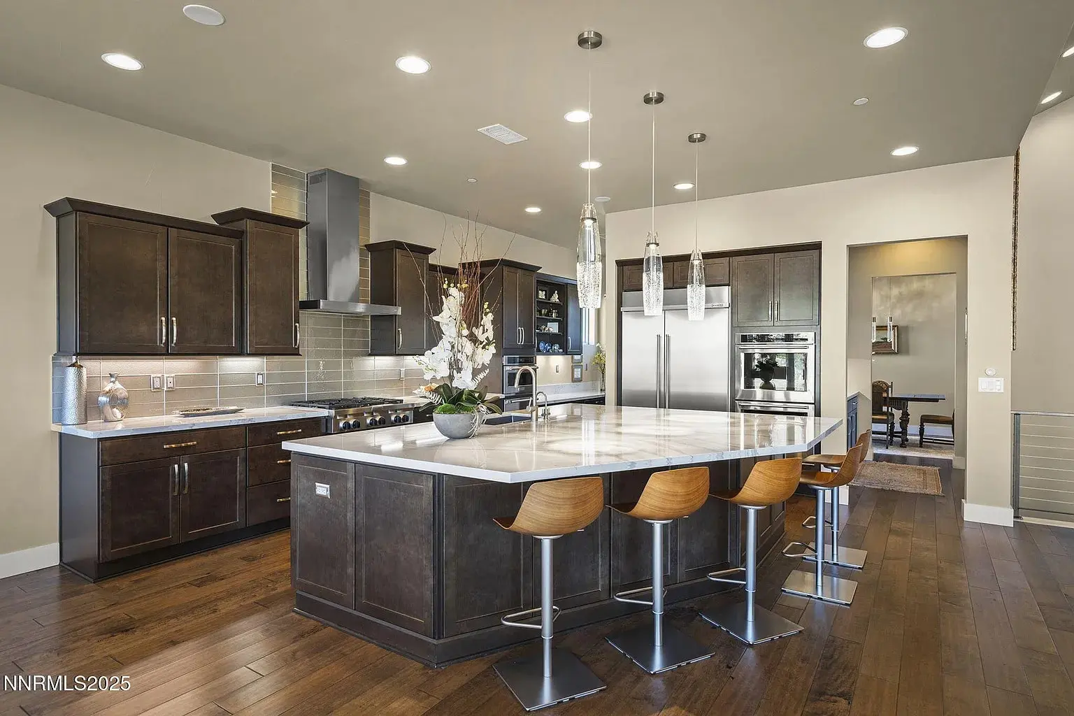 Modern kitchen with dark wood cabinets, large island, bar stools, and stainless steel appliances.