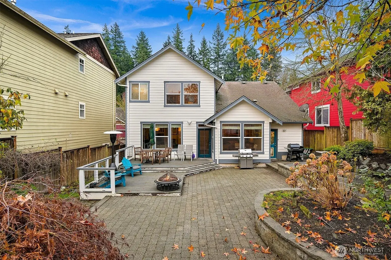 Backyard view of a two-story house with patio, fire pit, and surrounding trees.