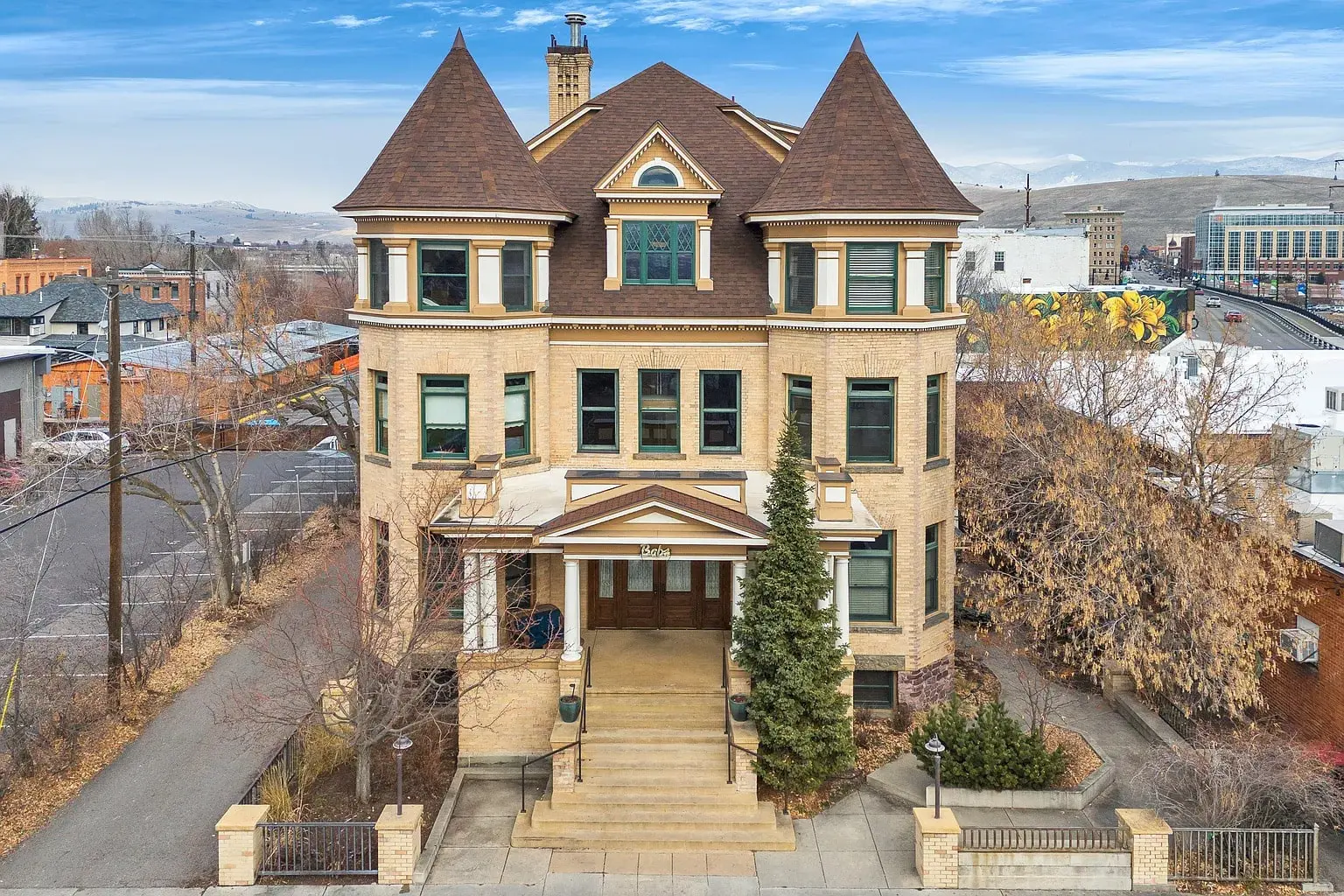 Historic multi-story brick building with a steep roof, surrounded by trees and urban landscape.