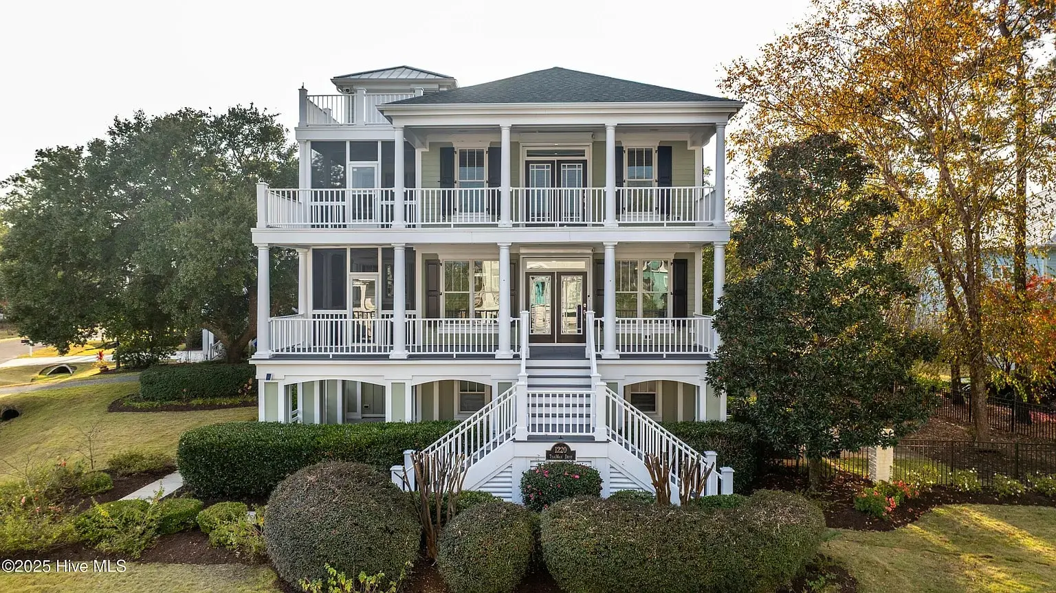 Three-story white house with multiple balconies, surrounded by trees and landscaped shrubs.
