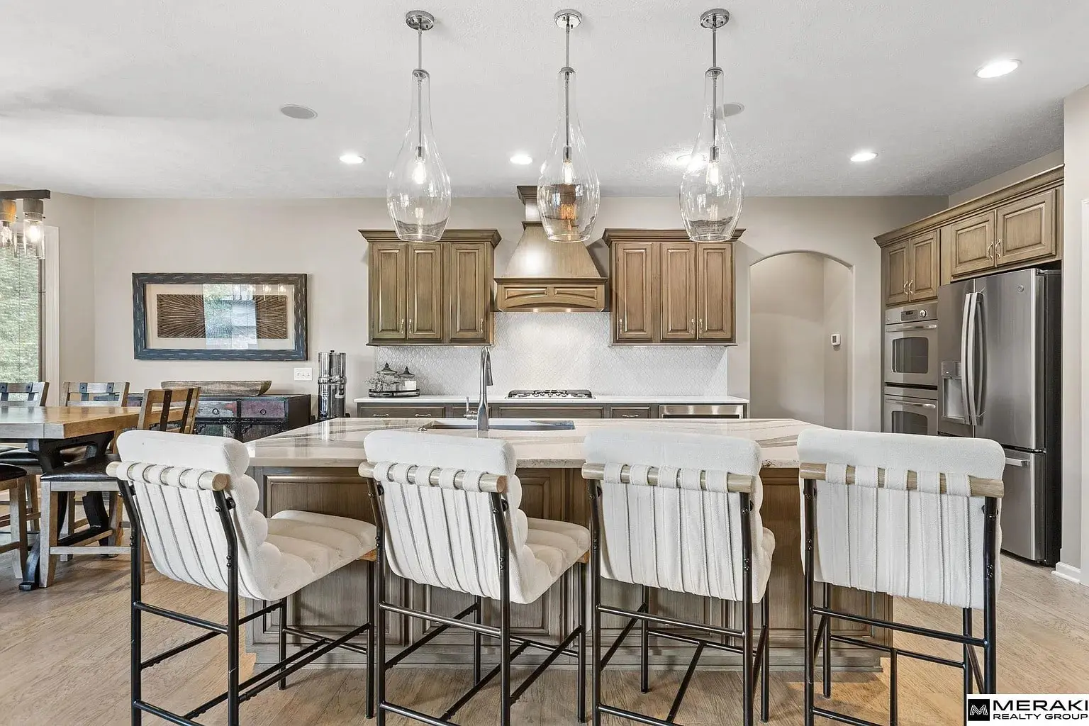 Modern kitchen with wooden cabinets, island with four cushioned stools, and stainless steel appliances.