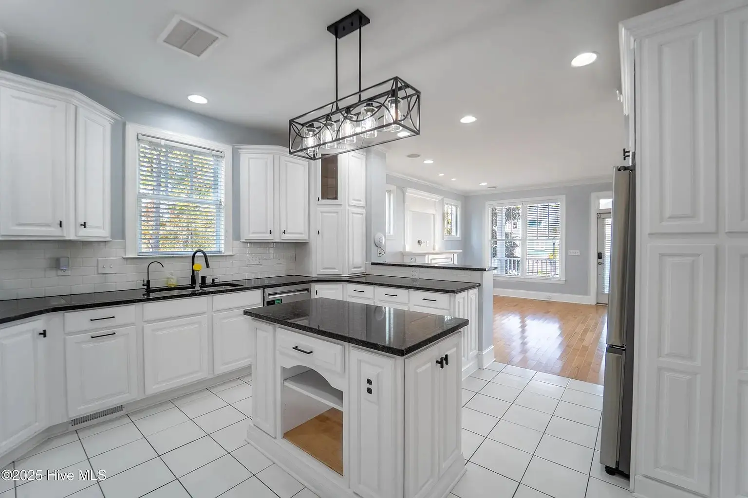 Modern kitchen with white cabinets, black countertops, island, and hanging light fixture. Bright and spacious.