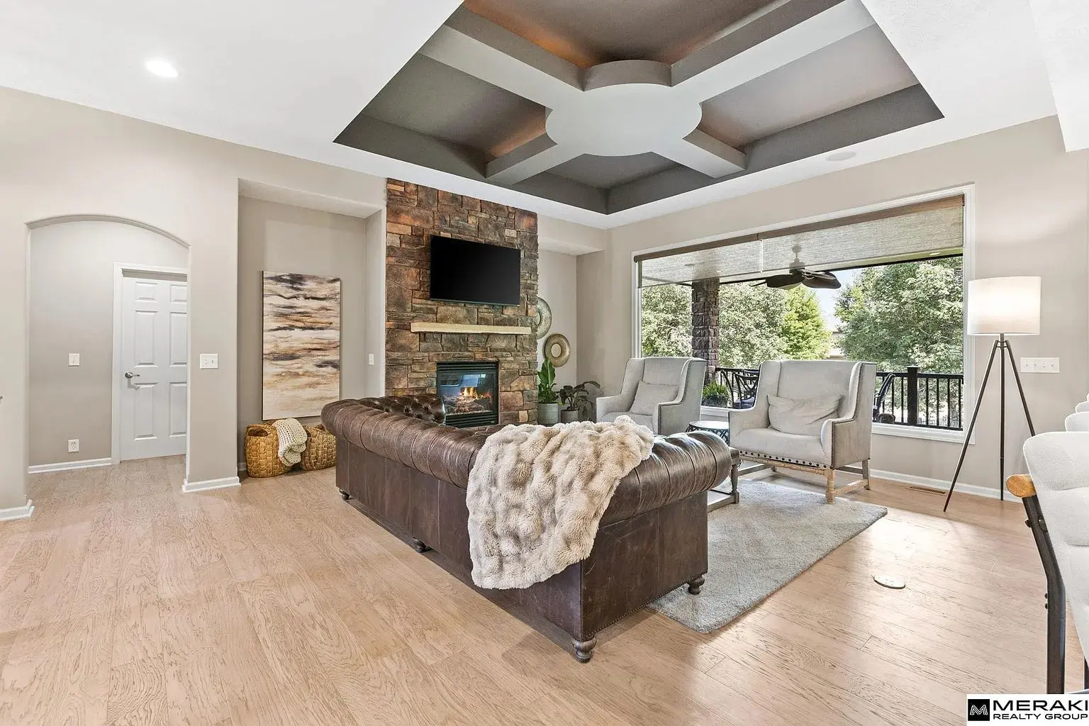 Living room with a leather sofa, stone fireplace, and large window overlooking trees.