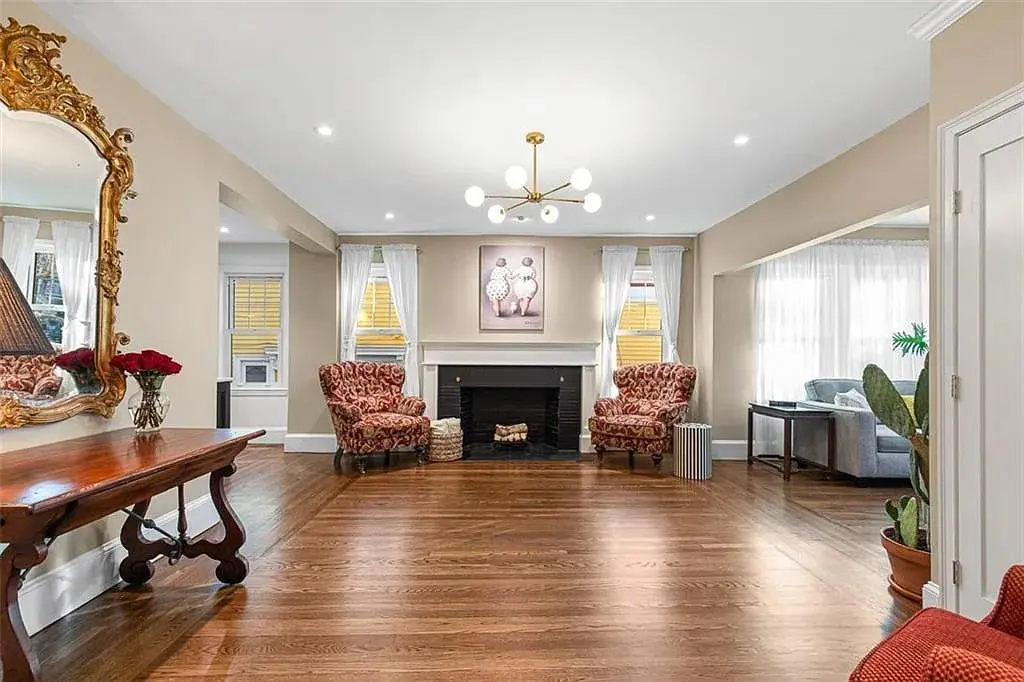 Elegant living room with wooden floor, ornate mirror, chandelier, fireplace, and patterned armchairs.
