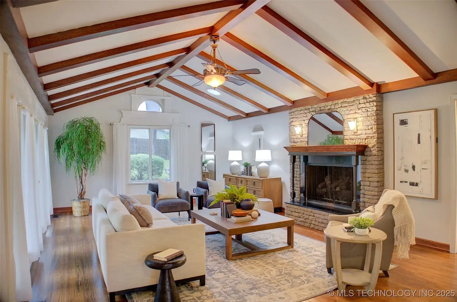 Spacious living room with vaulted ceiling, wooden beams, stone fireplace, and modern furniture.