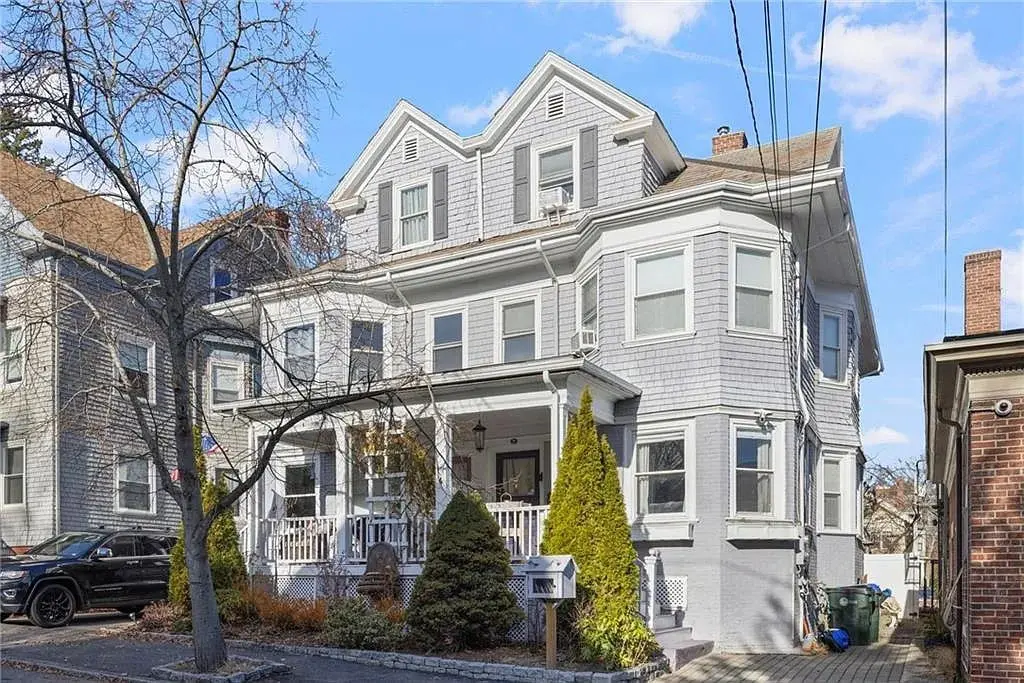 Large gray three-story house with a porch, surrounded by trees and a driveway.