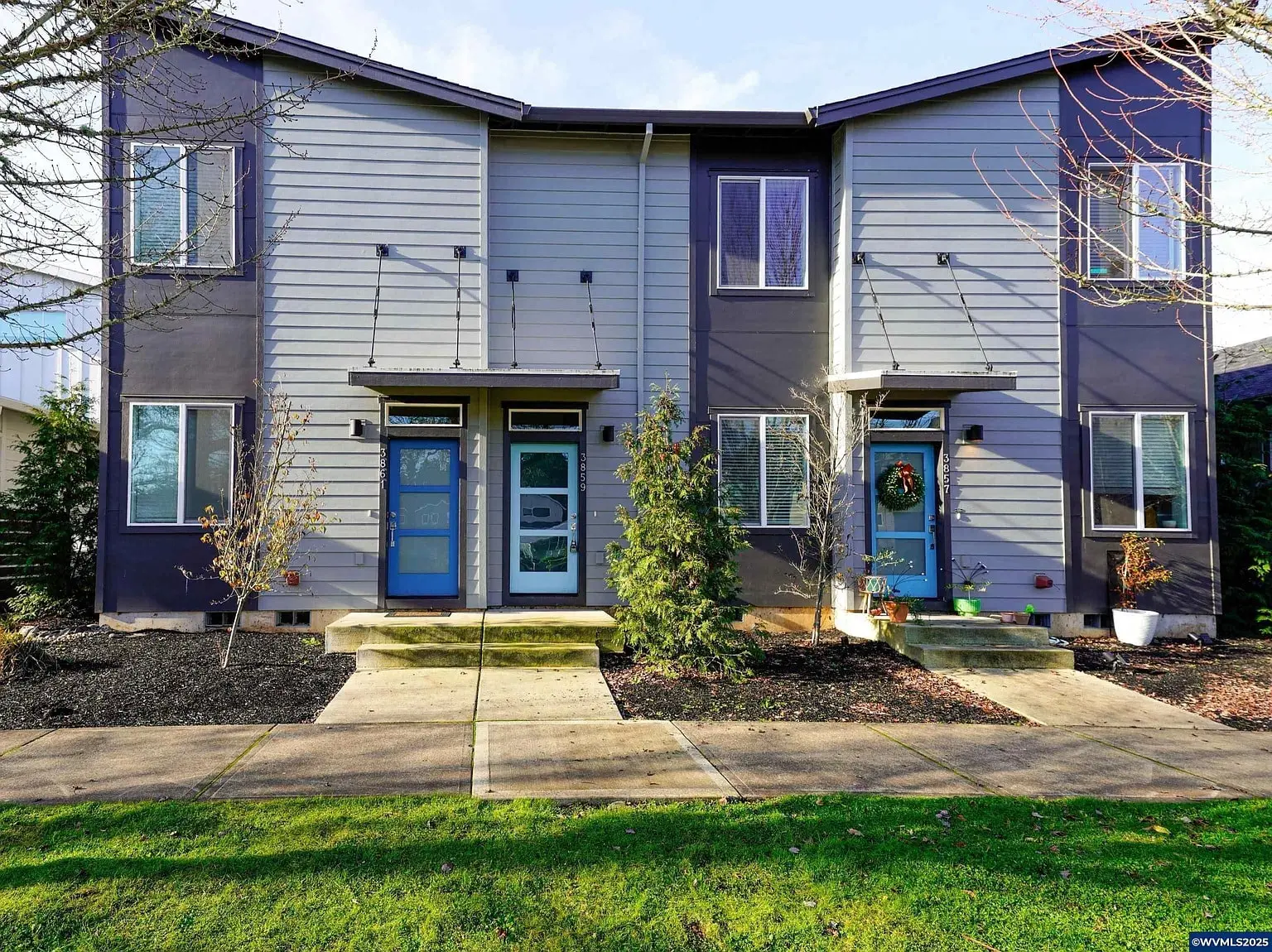 Two modern townhouses with blue doors, small front yards, and a shared pathway.