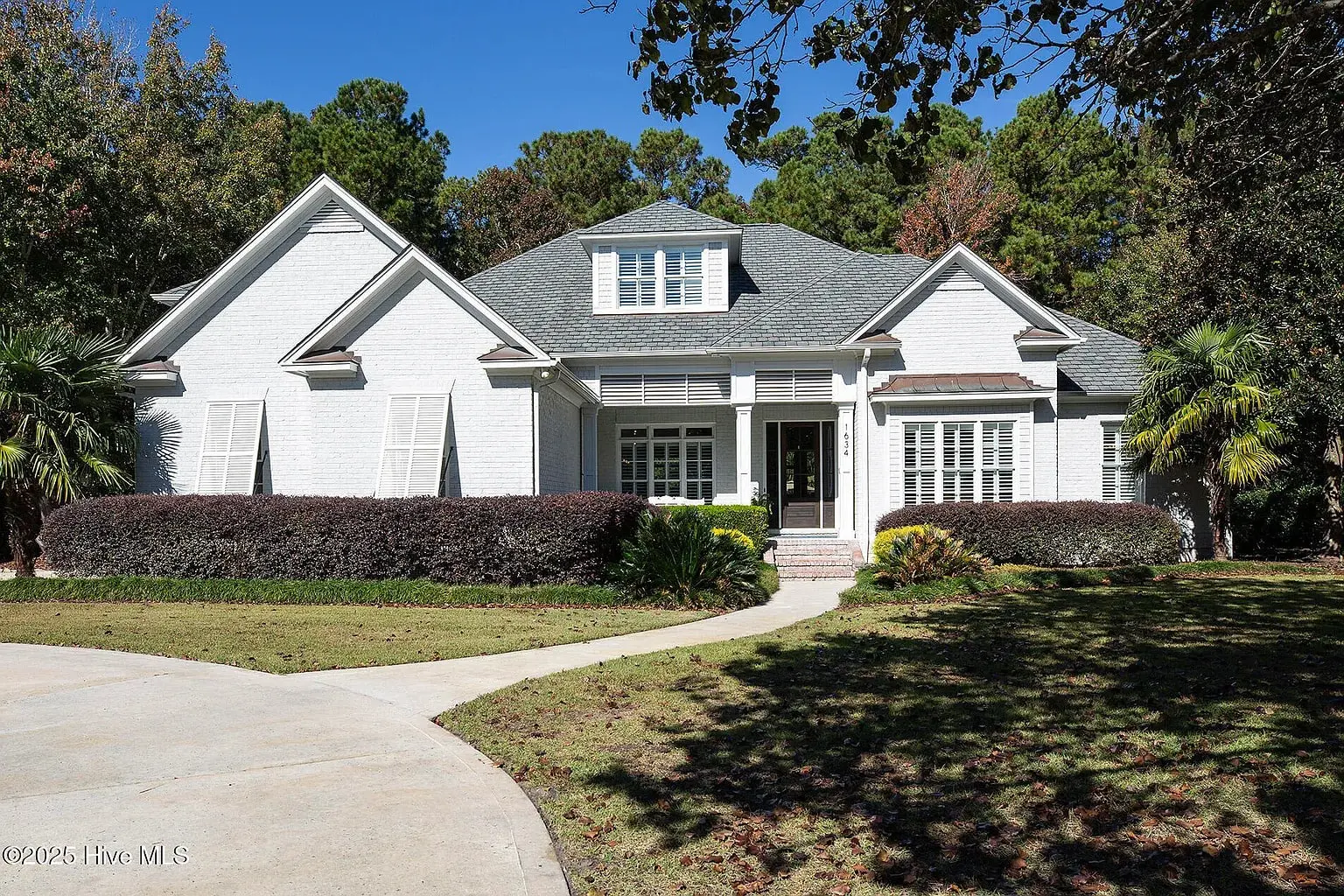 White brick house with a gray roof, surrounded by trees and a curved driveway.