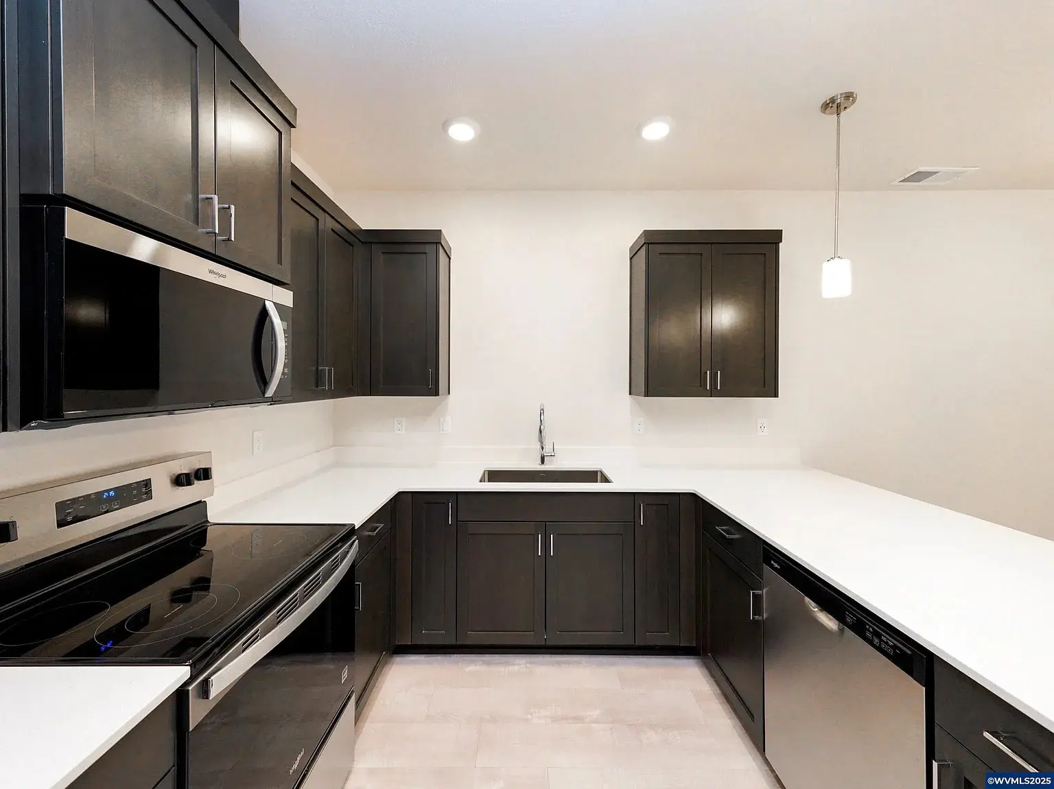 Modern kitchen with dark cabinets, white countertops, stainless steel appliances, and recessed lighting.