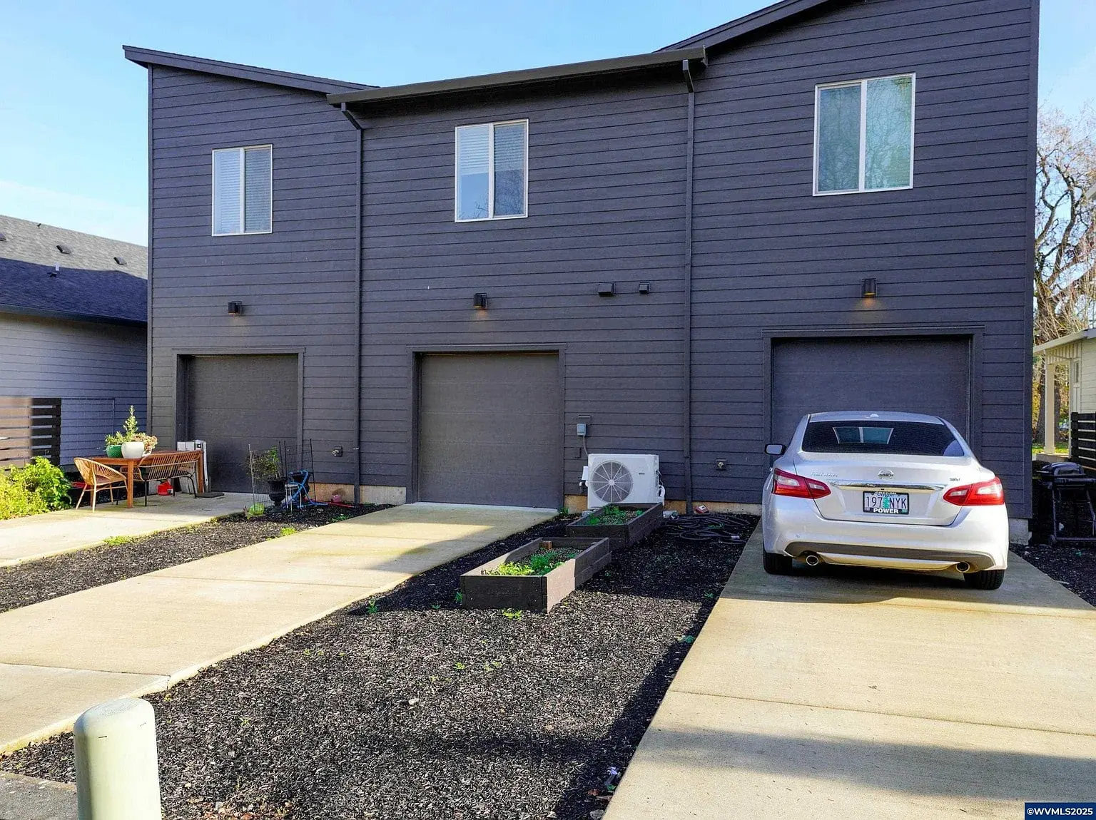 Modern duplex with two garage doors, a parked car, and small garden beds in front.