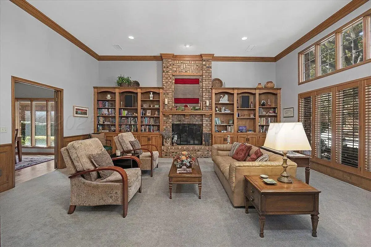Spacious living room with brick fireplace, bookshelves, armchairs, sofa, and large windows.