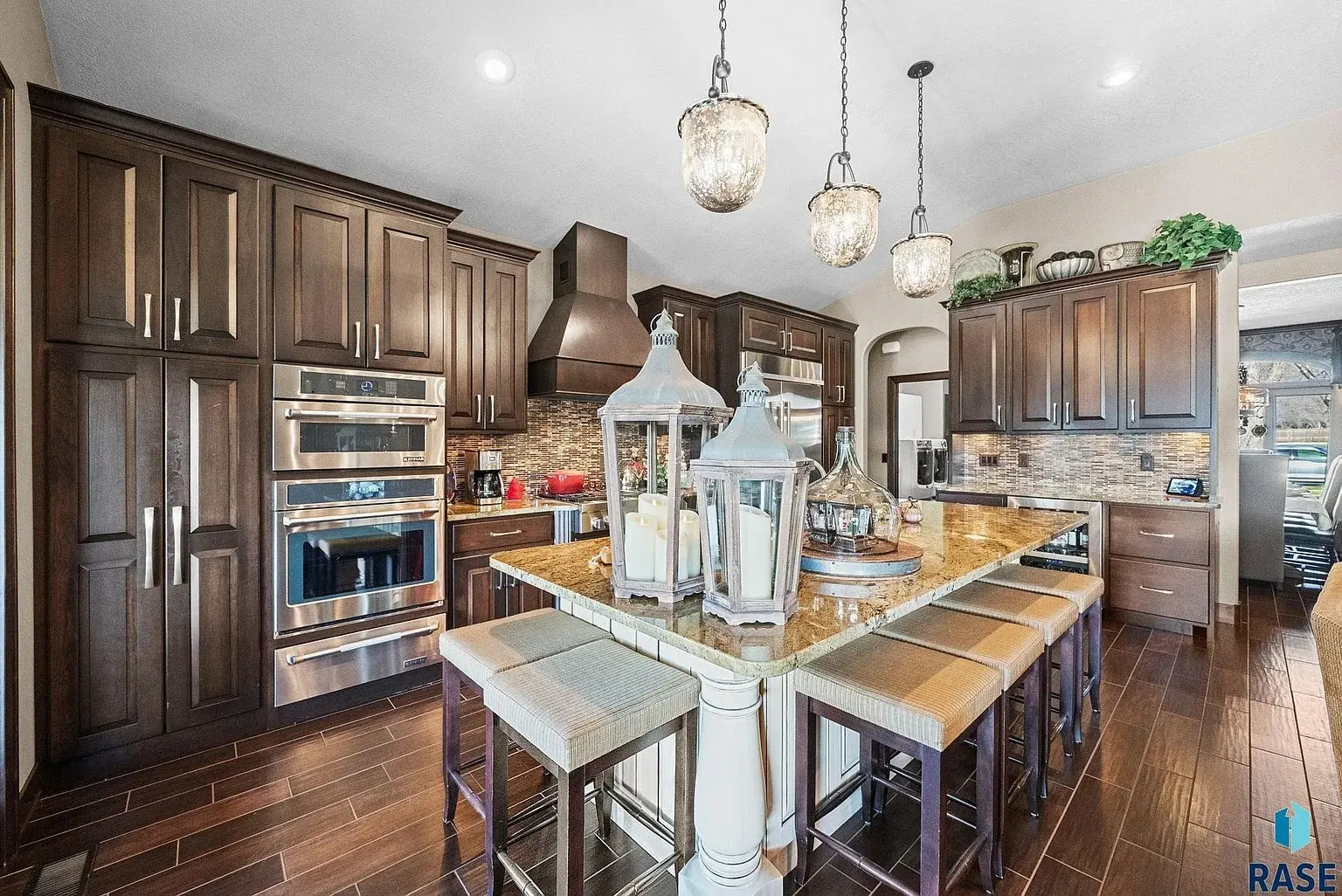 Modern kitchen with dark wood cabinets, island with stools, pendant lights, and stainless steel appliances.