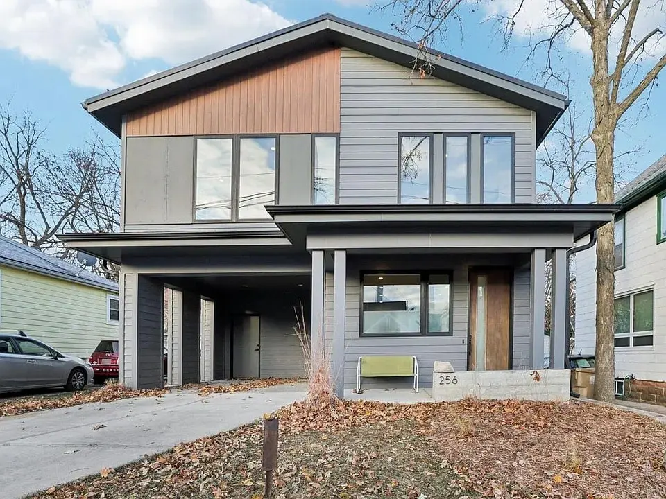 Modern two-story house with large windows, gray siding, and a covered driveway.