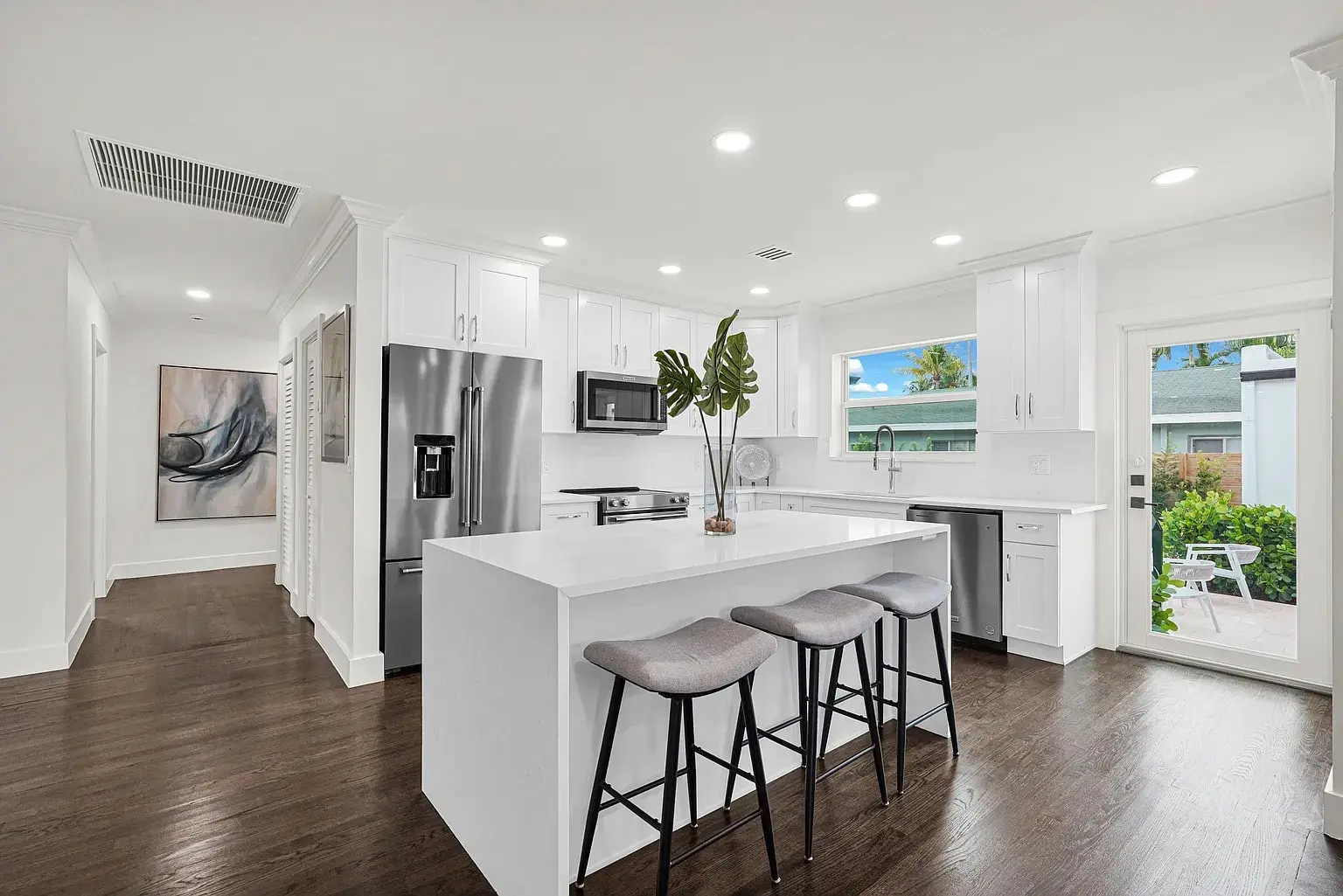 Modern kitchen with white cabinets, stainless steel appliances, island with stools, and large window.