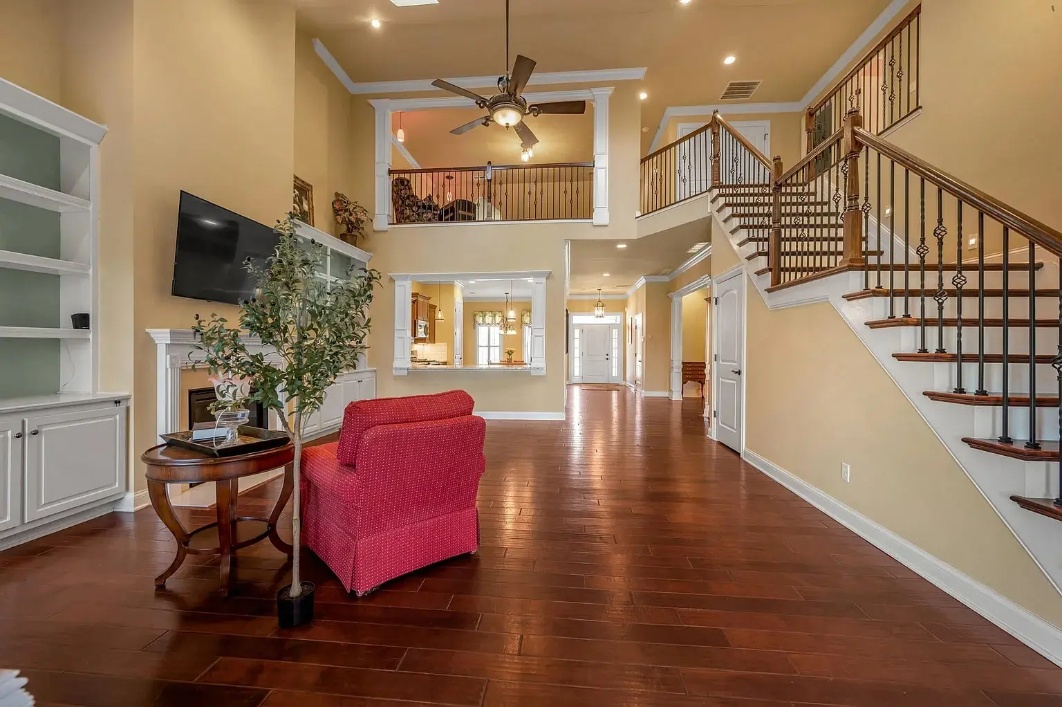 Spacious living room with hardwood floors, red armchair, staircase, and wall-mounted TV.