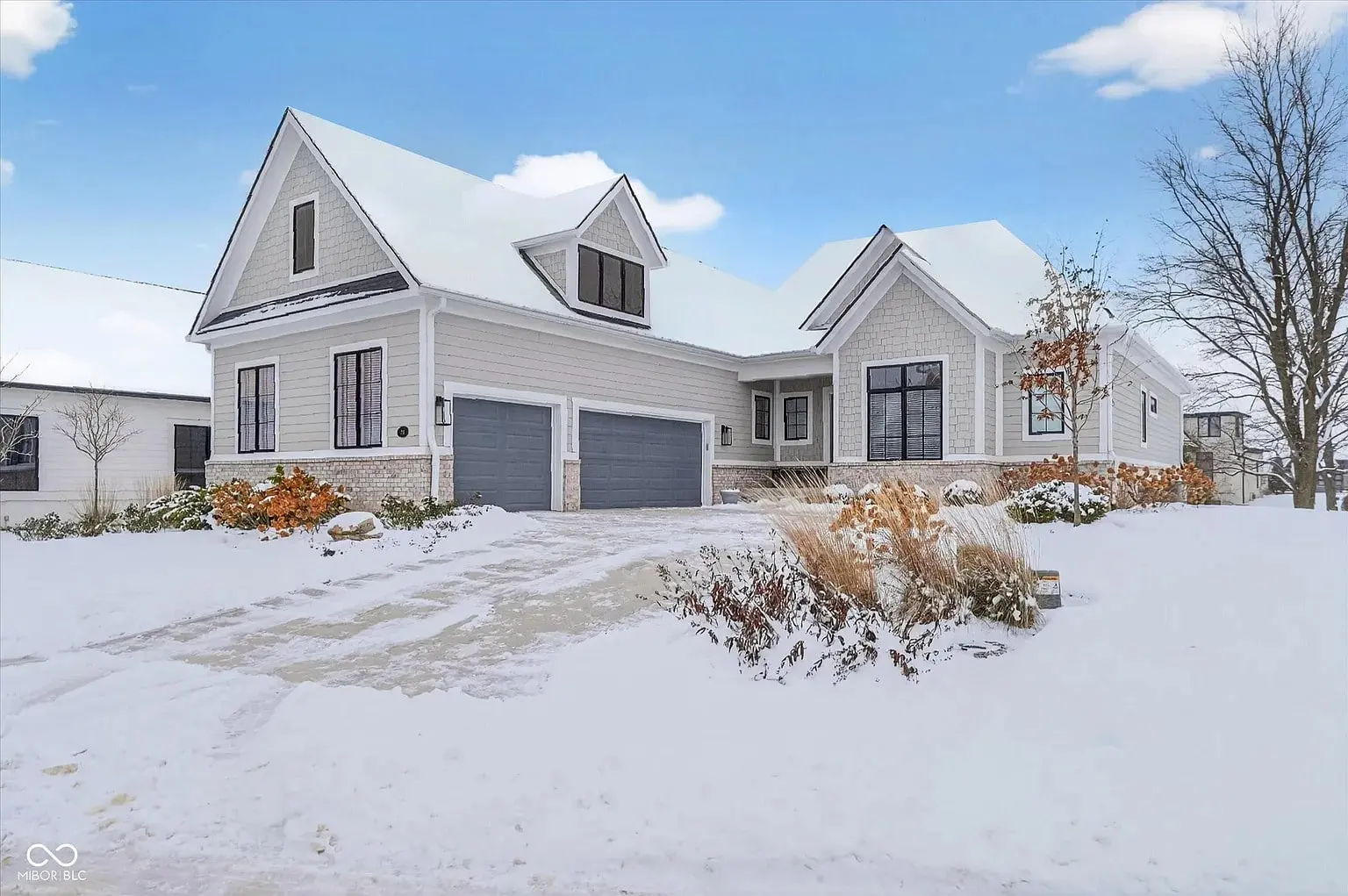 Modern house with snow-covered yard, two-car garage, and clear blue sky.