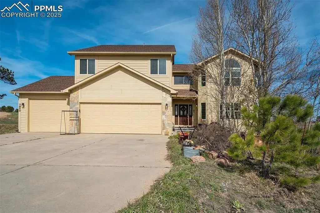 Two-story beige house with a three-car garage and surrounding trees.