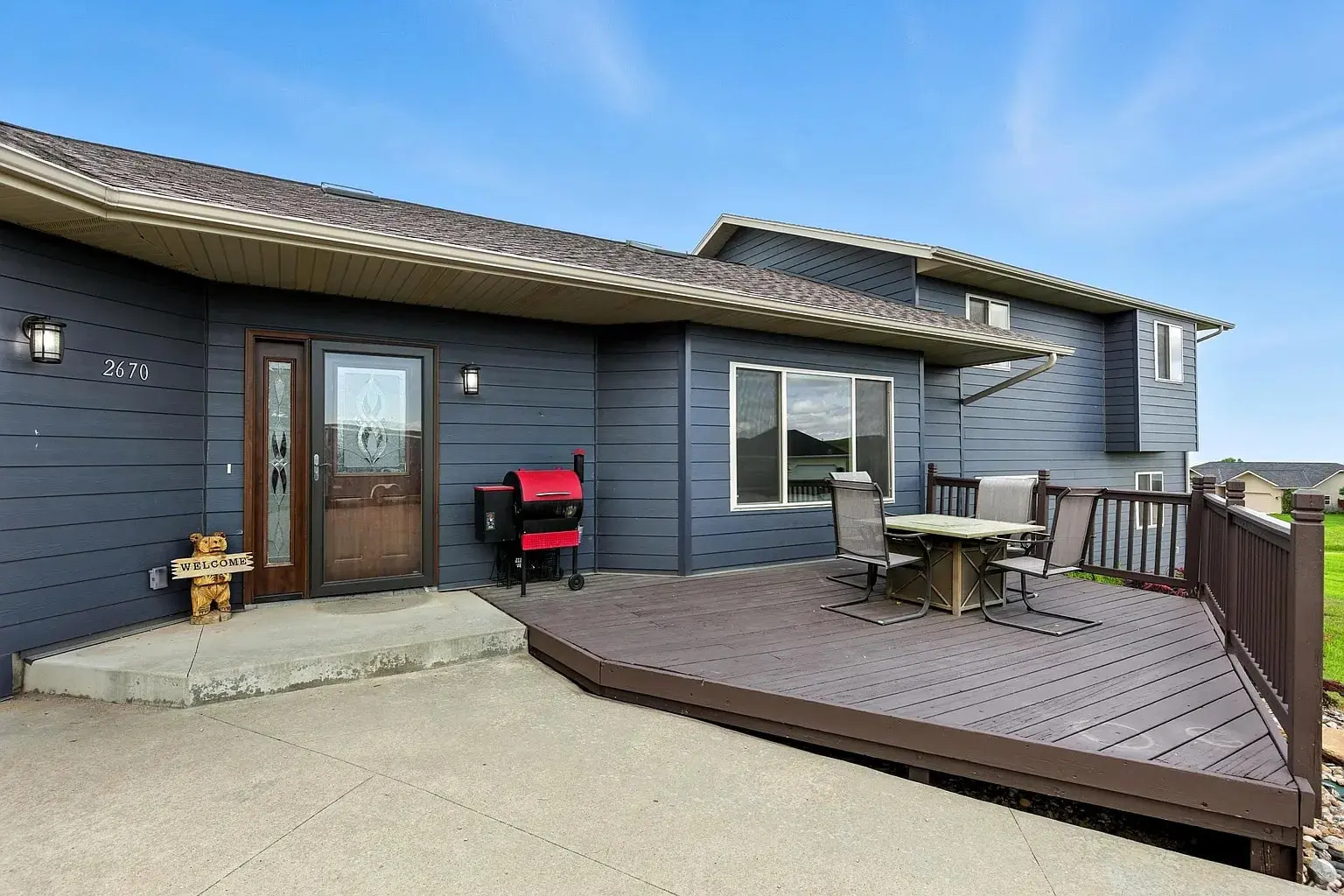 Modern house with a wooden deck, outdoor dining set, and a red grill.