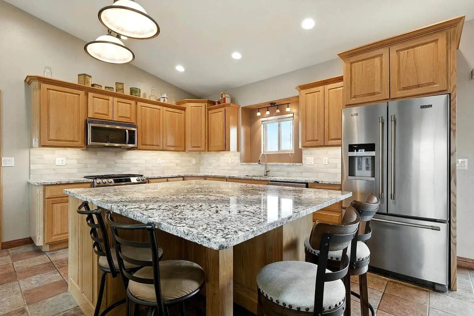 Spacious kitchen with wooden cabinets, granite countertops, stainless steel appliances, and bar seating.