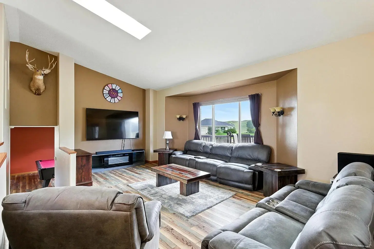 Spacious living room with sofas, large TV, deer head mount, and window view of mountains.