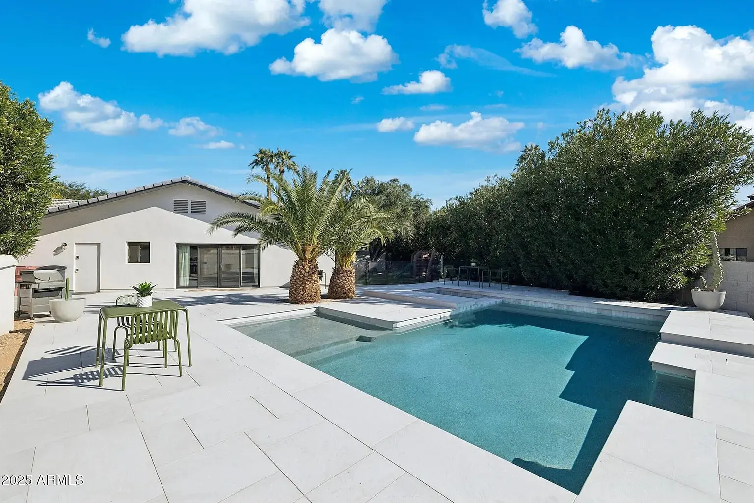 Backyard with a modern pool, palm trees, and patio furniture under a clear blue sky.