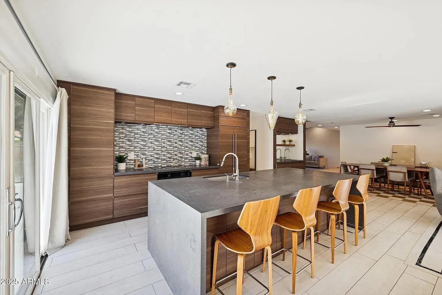 Modern kitchen with large island, wooden bar stools, pendant lights, and a patterned backsplash.
