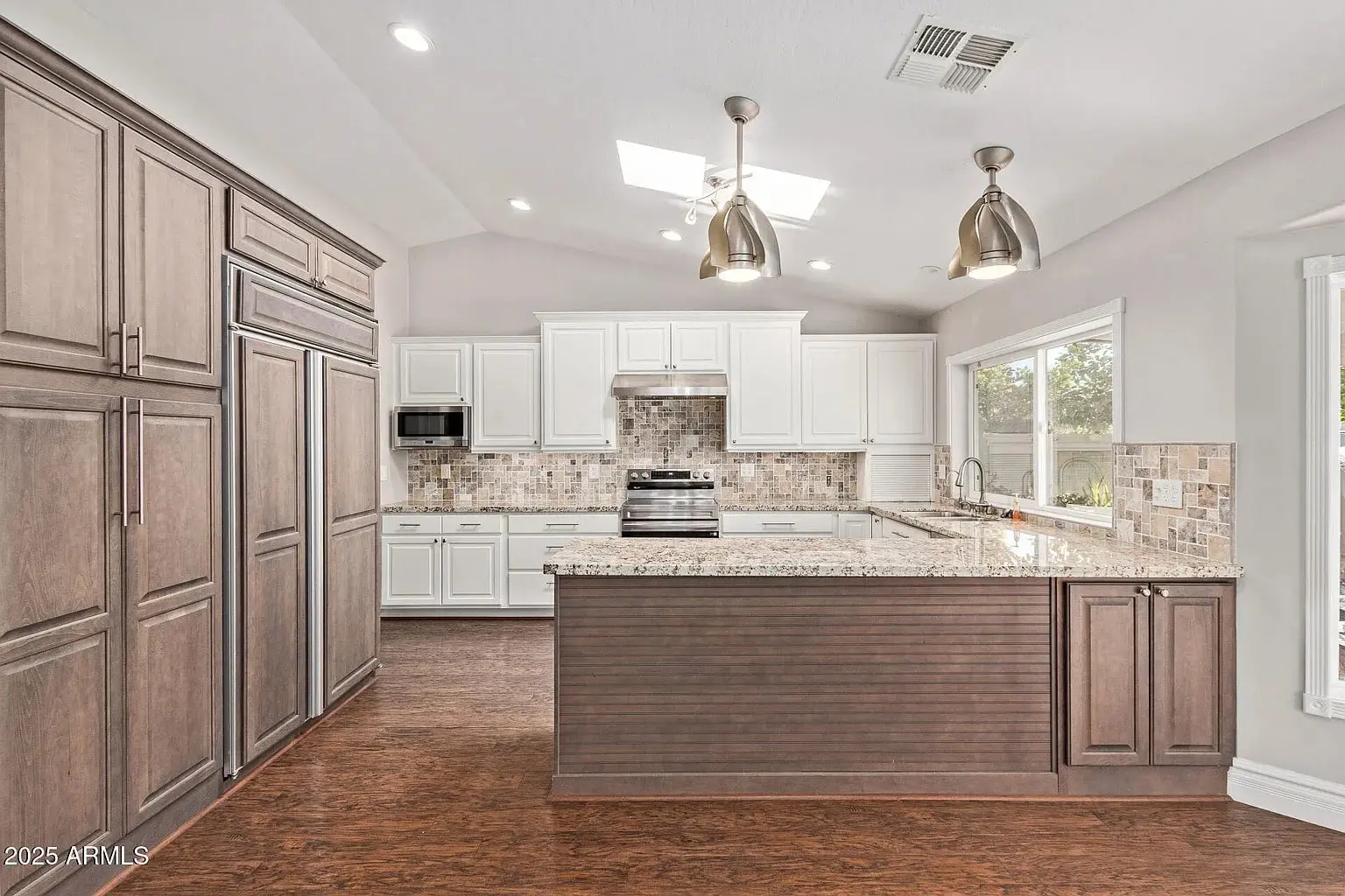 Modern kitchen with white cabinets, stainless steel appliances, large island, and wood flooring.