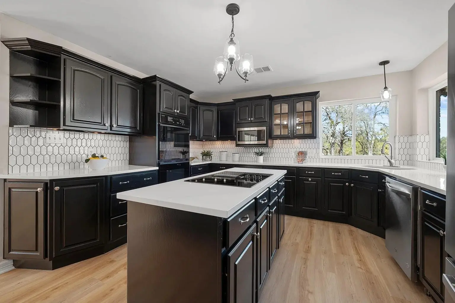 Modern kitchen with black cabinets, white countertops, hexagonal tile backsplash, and wooden floor.