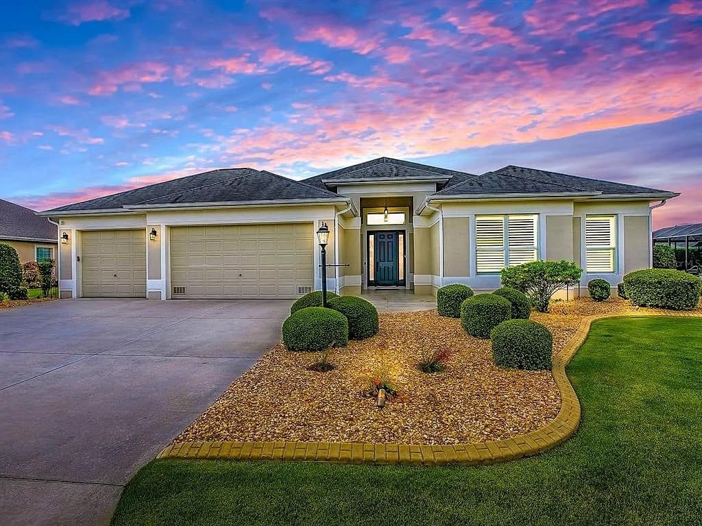Single-story house with a three-car garage, landscaped front yard, and vibrant sunset sky.