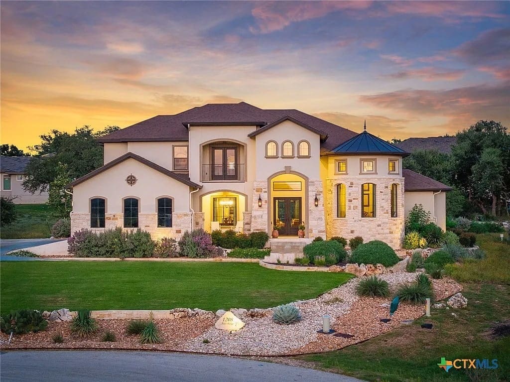 Large two-story house with stone and stucco exterior, surrounded by landscaped garden at sunset.