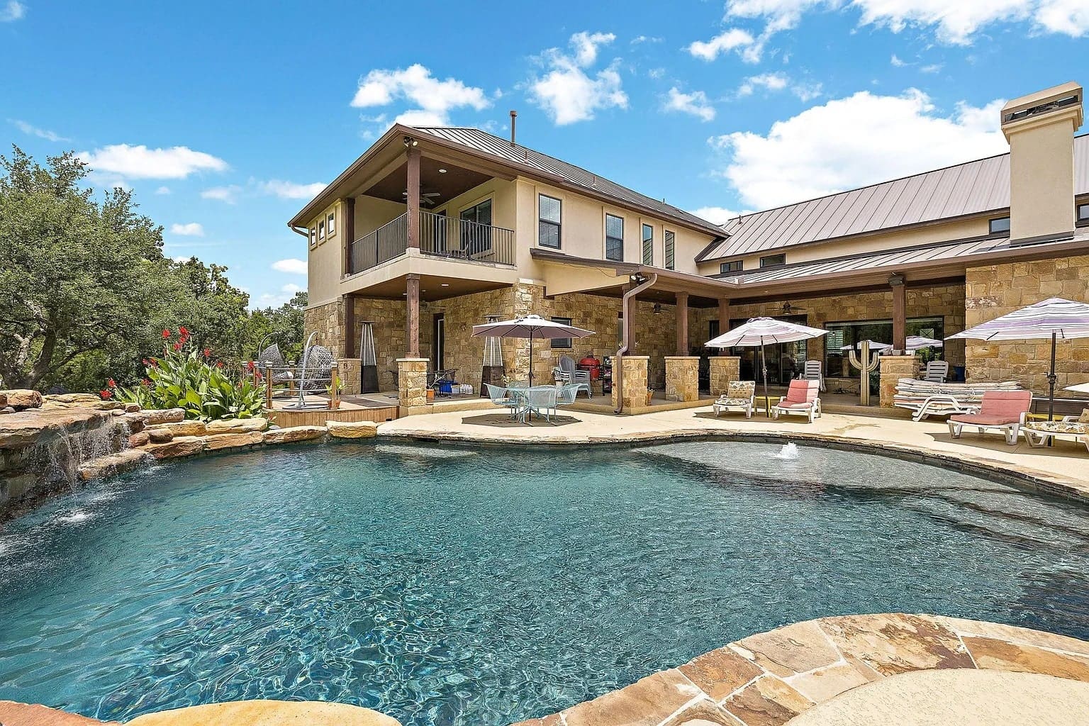 Luxury house with a large outdoor pool, patio, and lounge chairs under umbrellas.