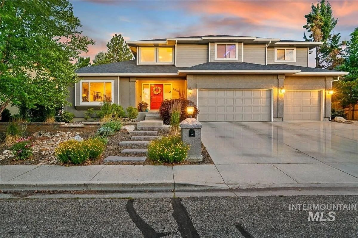 Two-story suburban house with a three-car garage and landscaped front yard at sunset.