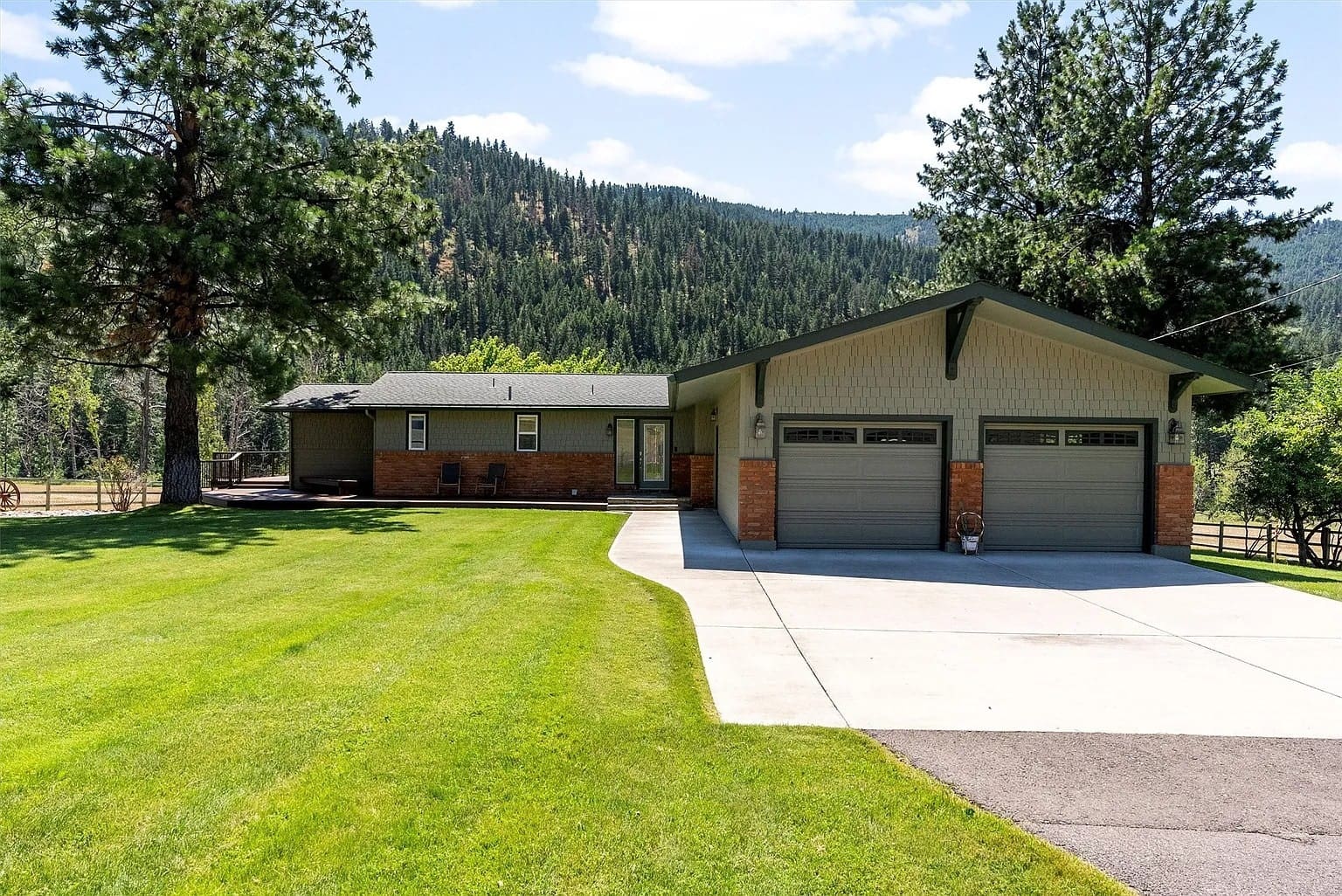 Single-story house with two-car garage, surrounded by trees and mountains, on a sunny day.