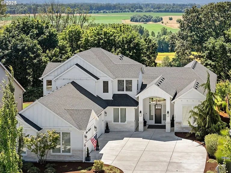 Large white house with a dark roof, surrounded by trees and fields in the background.