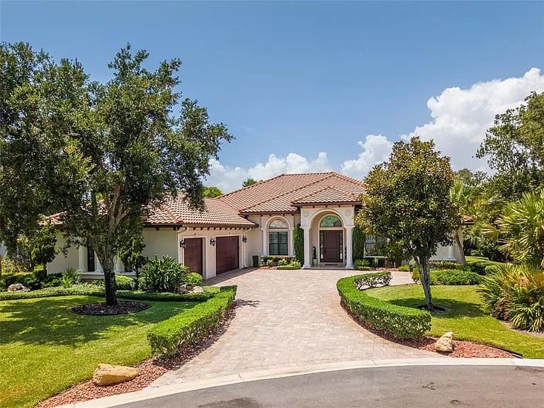 Single-story house with a tiled roof, surrounded by trees and a paved driveway.