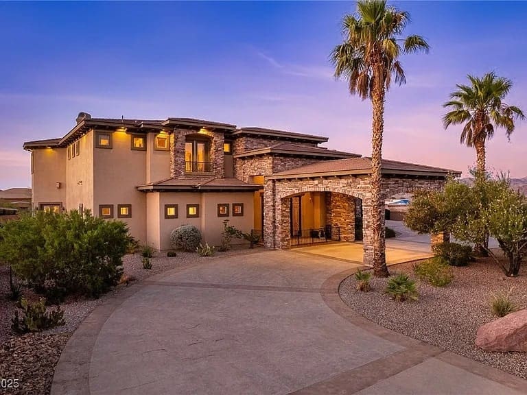 Modern two-story house with stone accents, palm trees, and a circular driveway at sunset.