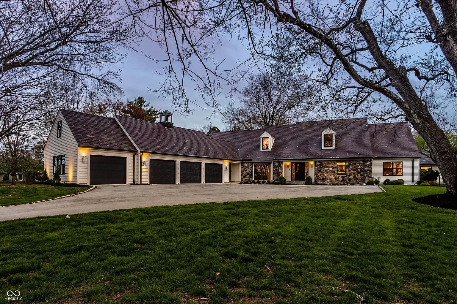 Large house with stone and wood exterior, multiple garages, surrounded by trees and grass.